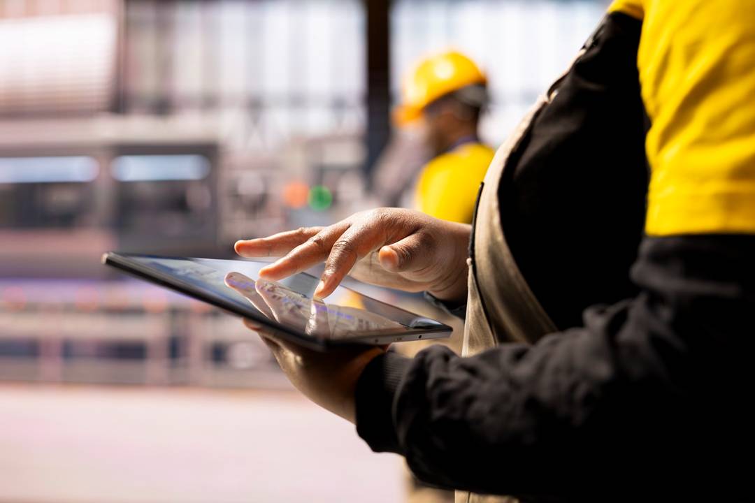 Tecnico consulta dati operativi su tablet per coordinare logistica integrata e reparti aziendali